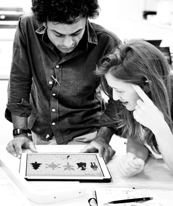 Black-and-white image of a man and a woman huddled over a digital tablet, both focused on illustrations on its screen.