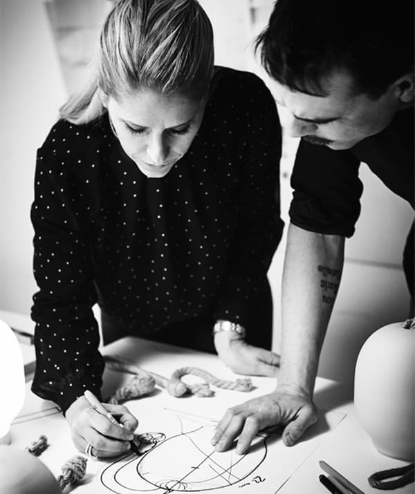 Black-and-white image of a woman and a man standing huddled over a table, both focused on a sketch the former is drawing.