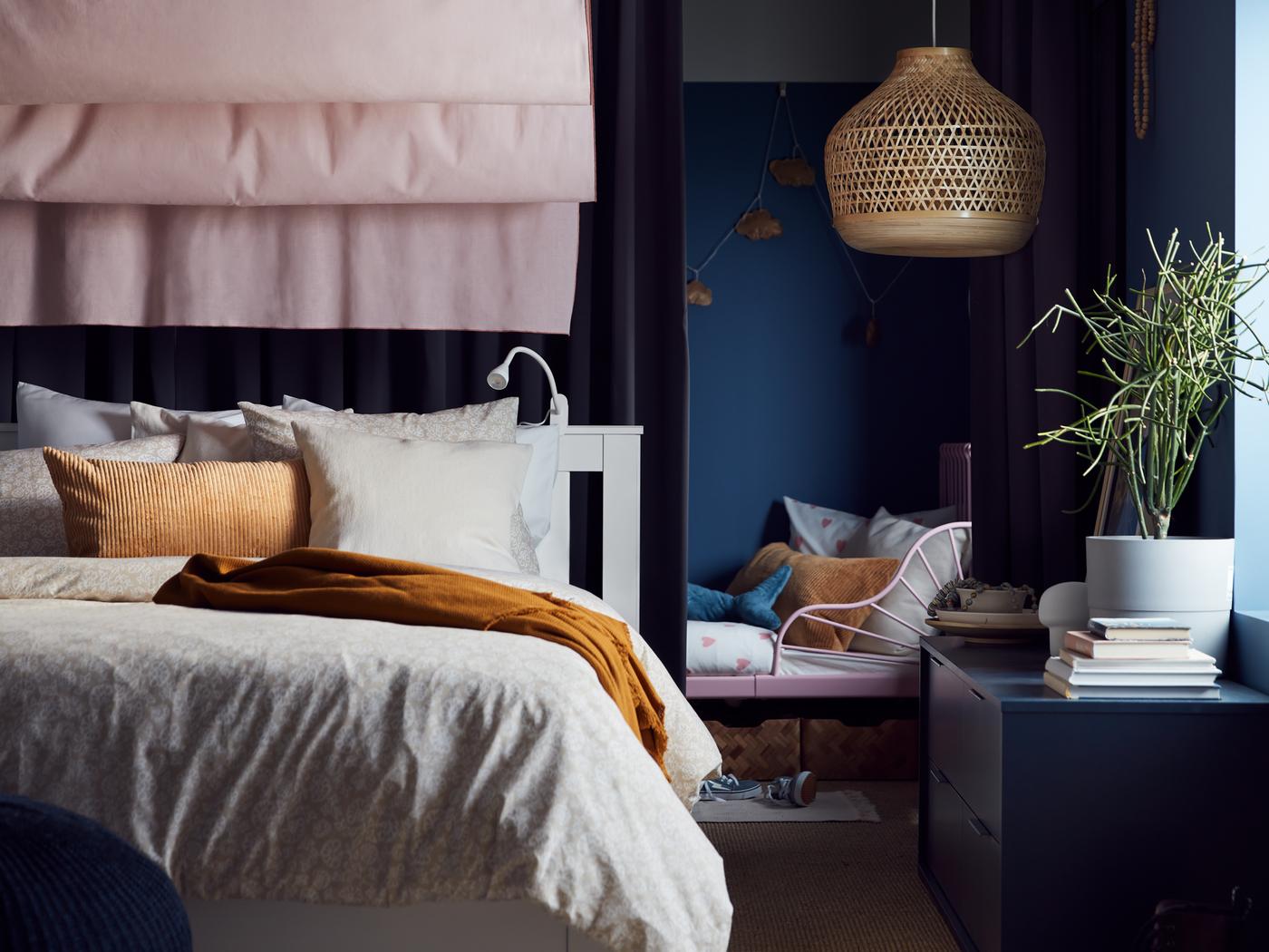 Blick auf ein weisses SONGESAND Bettgestell mit hellgrauer Bettwäsche. Auf dem Bett liegt ein OMTÄNKSAM Plaid, dahinter ist eine Hängeleuchte zu sehen.