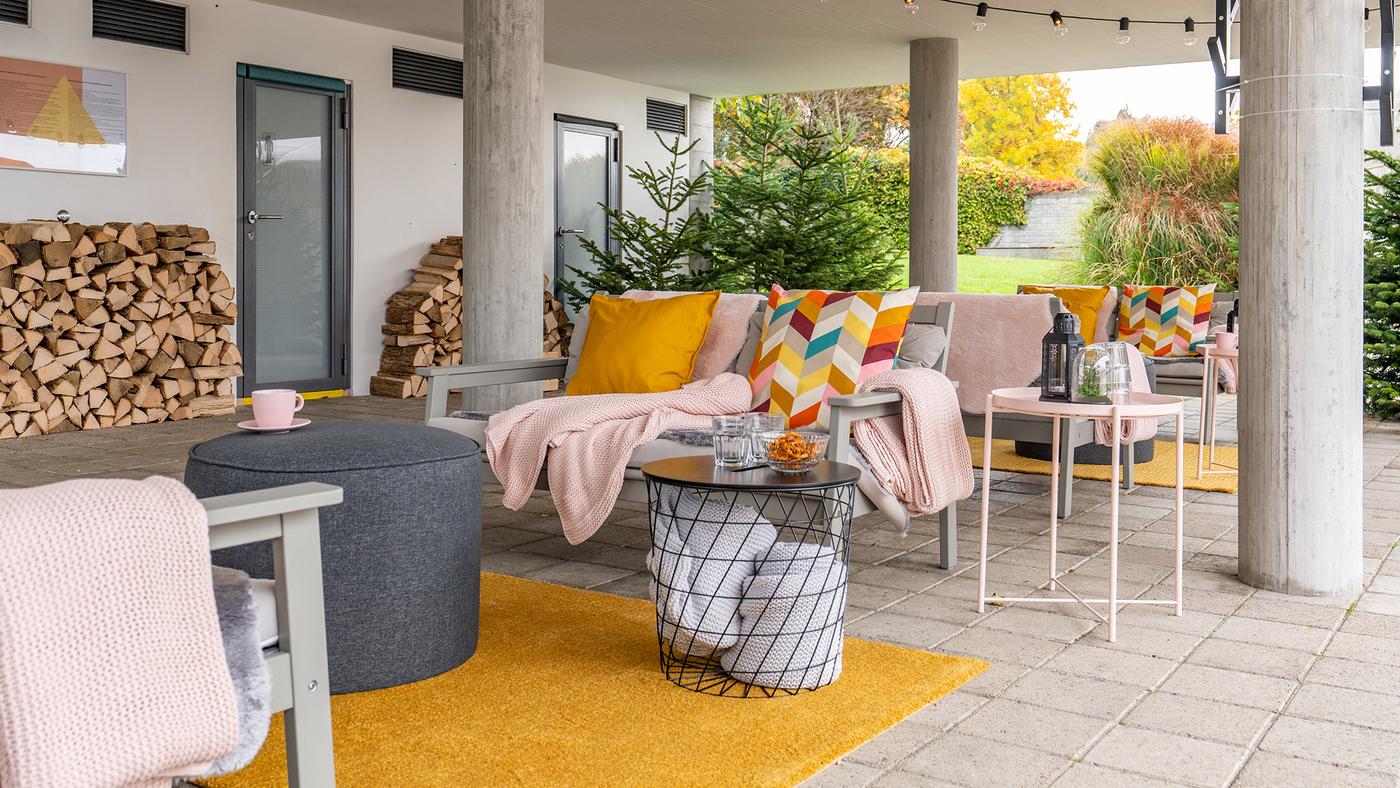 Blick auf eine grosse Terrasse mit Sitzbänken, auf denen Sitzpolster, Kissen und Decken liegen