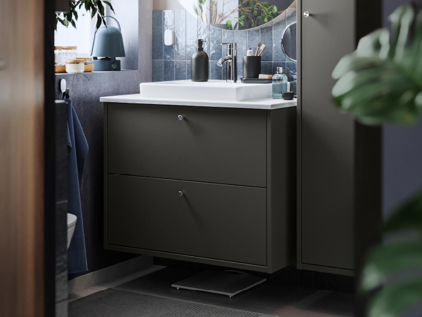 Blick auf einen dunkelgrauen HAVBÄCK Waschbeckenschrank mit Schubladen und Waschbecken neben einem dunkelgrauen Hochschrank. Über dem Waschbecken hängt ein Spiegel.
