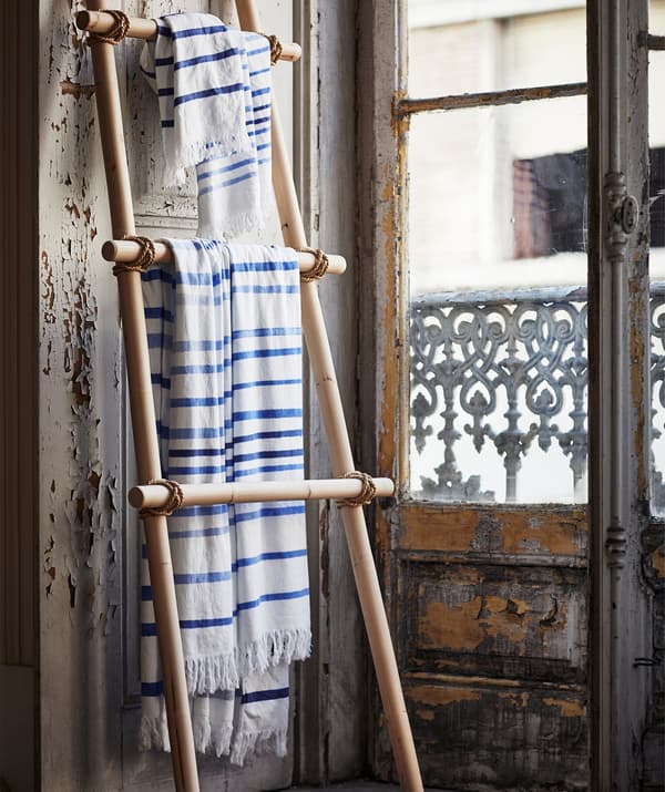 Blue and white striped TÄNKVÄRD fabric hanging on a wooden ladder shelf leaning against a wall.