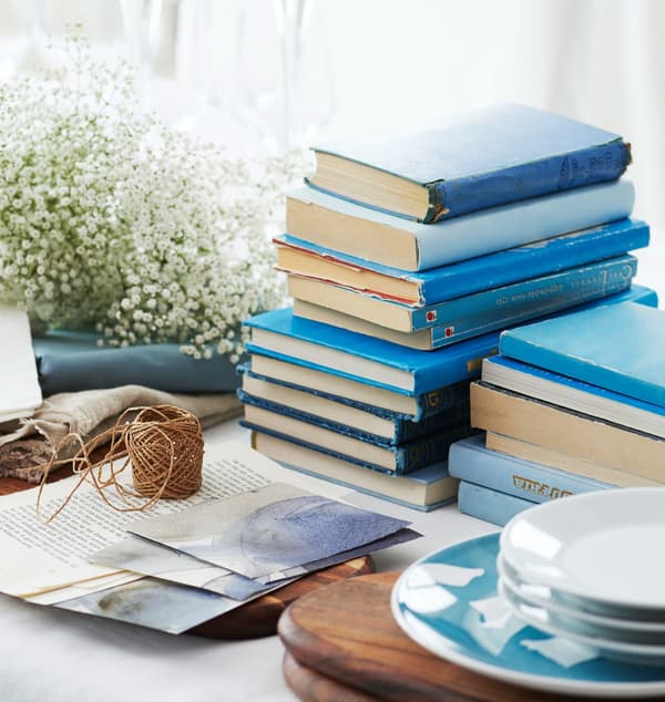 Blue books, baby’s breath flowers, and plates sit in the middle of the table waiting to be set.