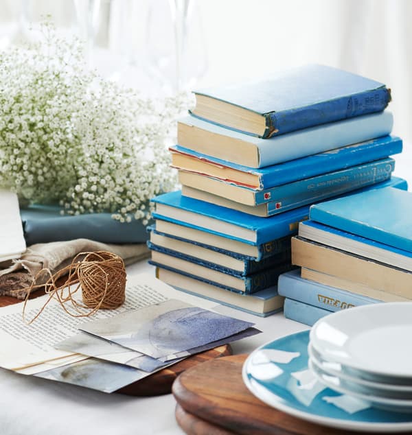 Blue books, baby’s breath flowers, and plates sit in the middle of the table waiting to be set.