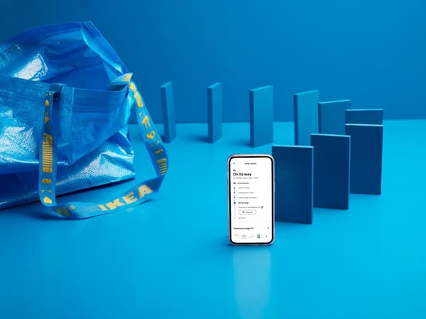 Blue dominoes, each the size of a smartphone, are lined up next to a blue IKEA FRAKTA bag. The one at the front is a switched-on smartphone.