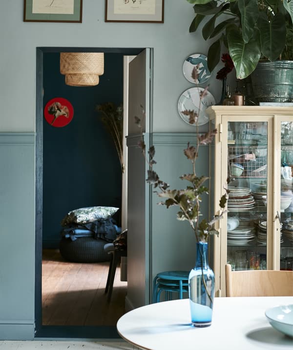 Blue glass vase on a table with view into the bedroom through an open door.