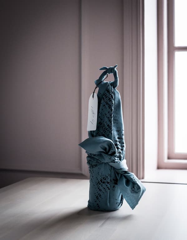 Blue IKEA DITTE fabric used to gift wrap a bottle, with a handwritten tag.