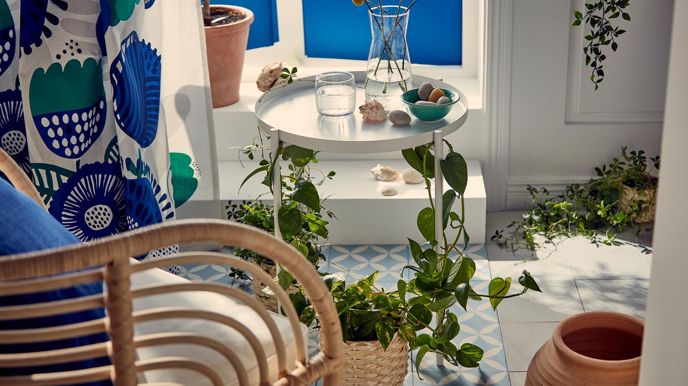 Blues and whites in a sunny spot just inside French balcony-style windows. Wicker armchair beside a plant-wrapped tray table.