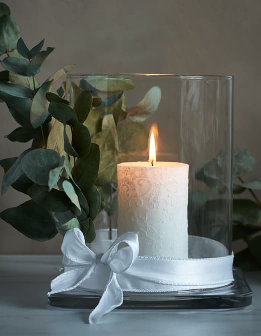 Bougie allumée présentée dans une lanterne en verre enrubannée.