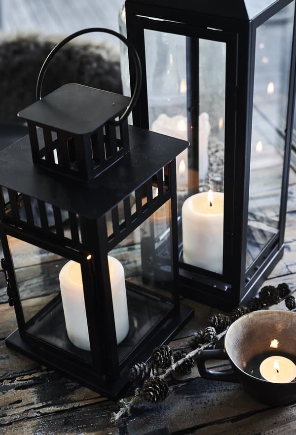 Bougies blocs blanches allumées dans une grande lanterne noire posée sur la table.