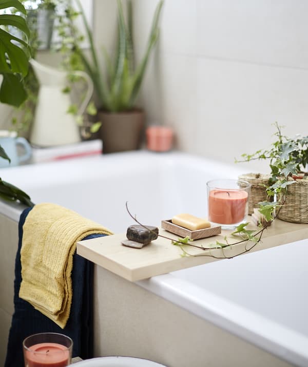 Bougies, savon et plantes sur une planche de bois posée sur une baignoire.
