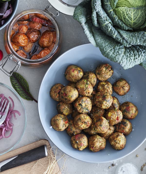 Boulettes végétariennes dans un saladier bleu, tomates rôties dans un bocal en verre et chou.