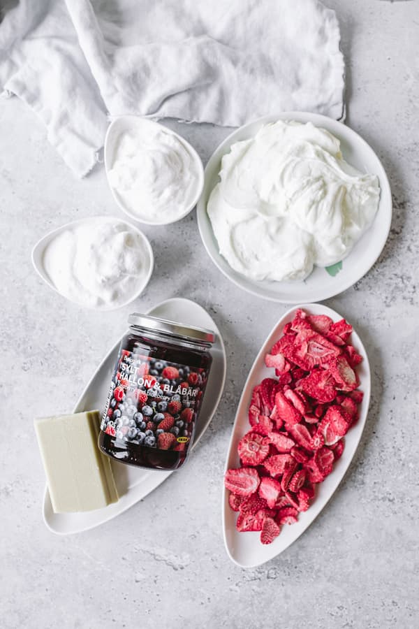 Bowls of yogurt or cream, jam, butter and sliced strawberries on light-colored surface.