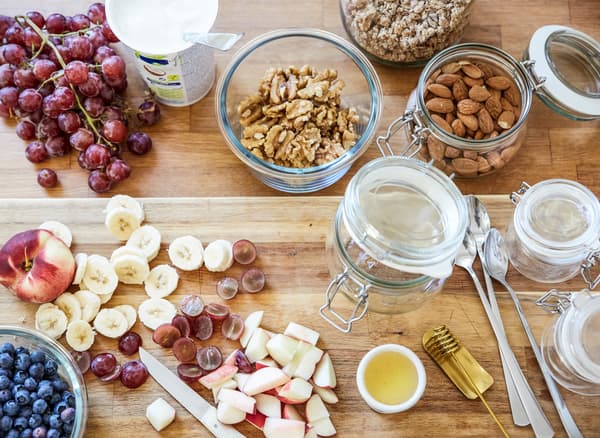 Breakfast ingredients, including chopped fruit, nuts and glass jars, laid out on a wooden countertop.