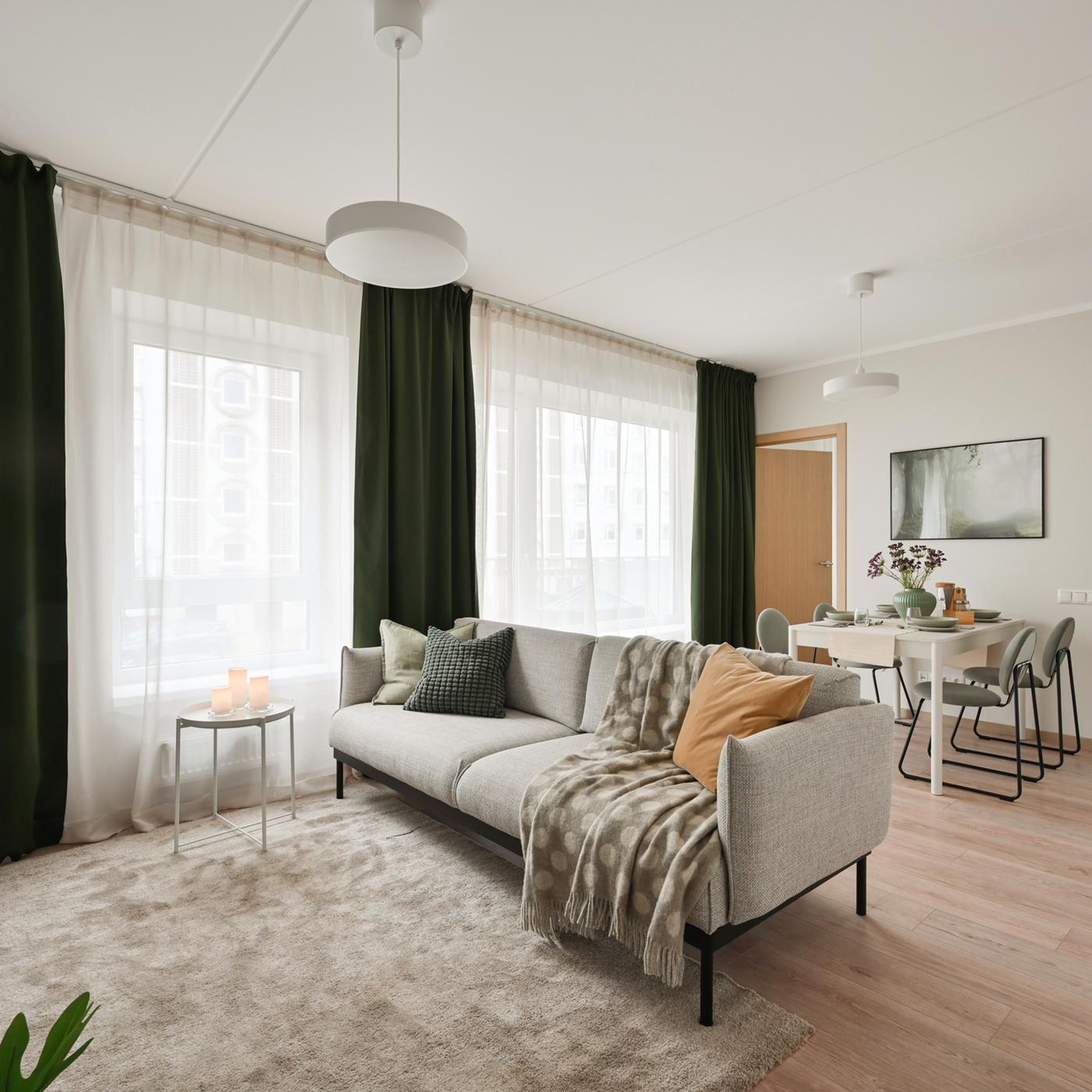 Bright and contemporary living room with soft neutral furnishings, deep green curtains, warm wooden accents, and large windows that create a calm and inviting atmosphere filled with natural light.
