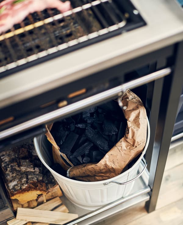 Bûches et charbon de bois pour le barbecue, rangés sur la tablette du bas du barbecue, vus d’en haut.
