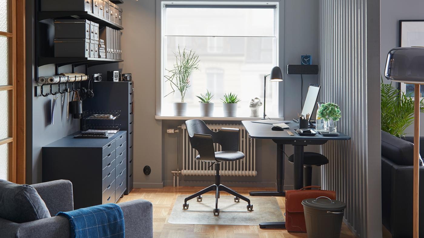 Bureau assis/debout BEKANT en linoleum bleu/noir dans un espace de travail aux couleurs coordonnées, avec un fauteuil de conférence et du rangement.
