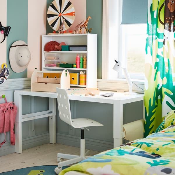 Bureau blanc, chaise de bureau enfant en blanc, lampe de table blanche et rideau à motif jungle.