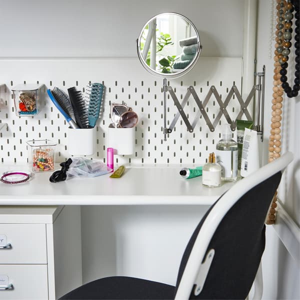 Bureau blanc sous un lit mezzanine. Un miroir est fixé au mur. Le nécessaire pour la coiffure est rangé sur le panneau perforé du lit mezzanine.