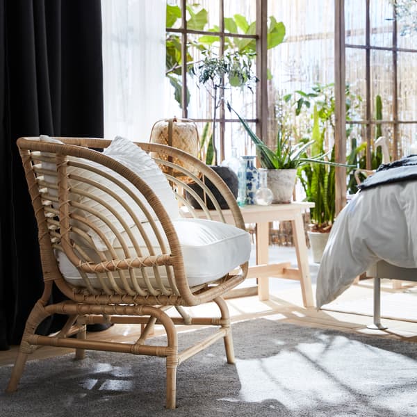 BUSKBO rattan chair with white cushions, dark grey and white curtains, a bench, green plants and a grey rug.