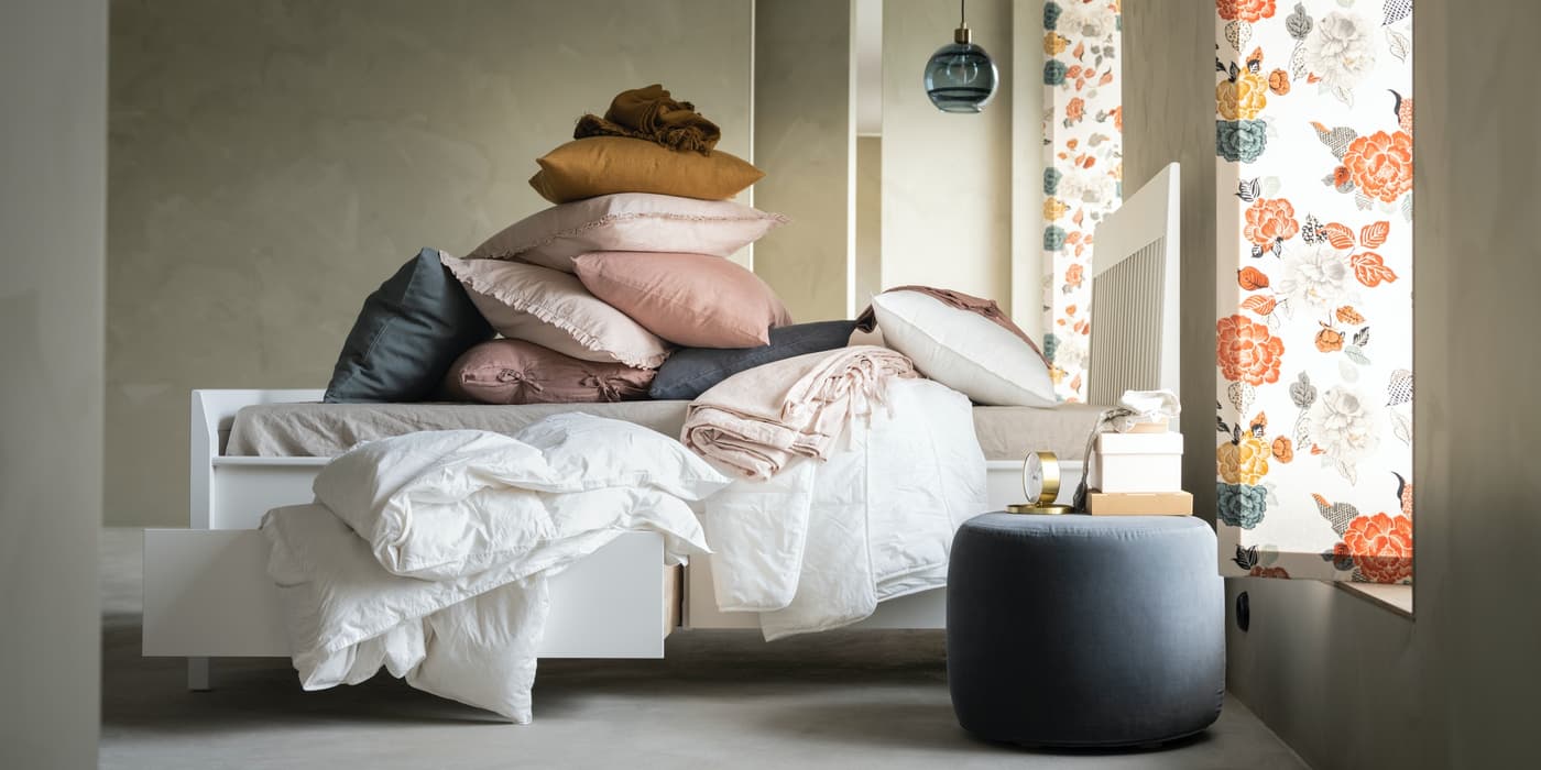 Cama blanca MALM cona almacenamiento, cubierta con ropa de cama y cojines de distintos colores.
