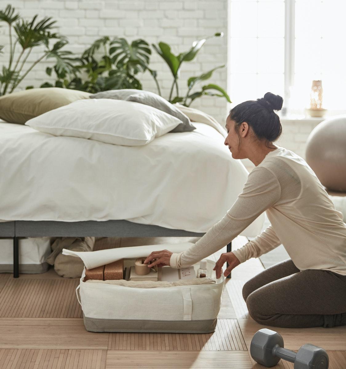 Cama con cajones abajo LACKISAR blancos con gris. Una mujer guardando sus cosas ahí.