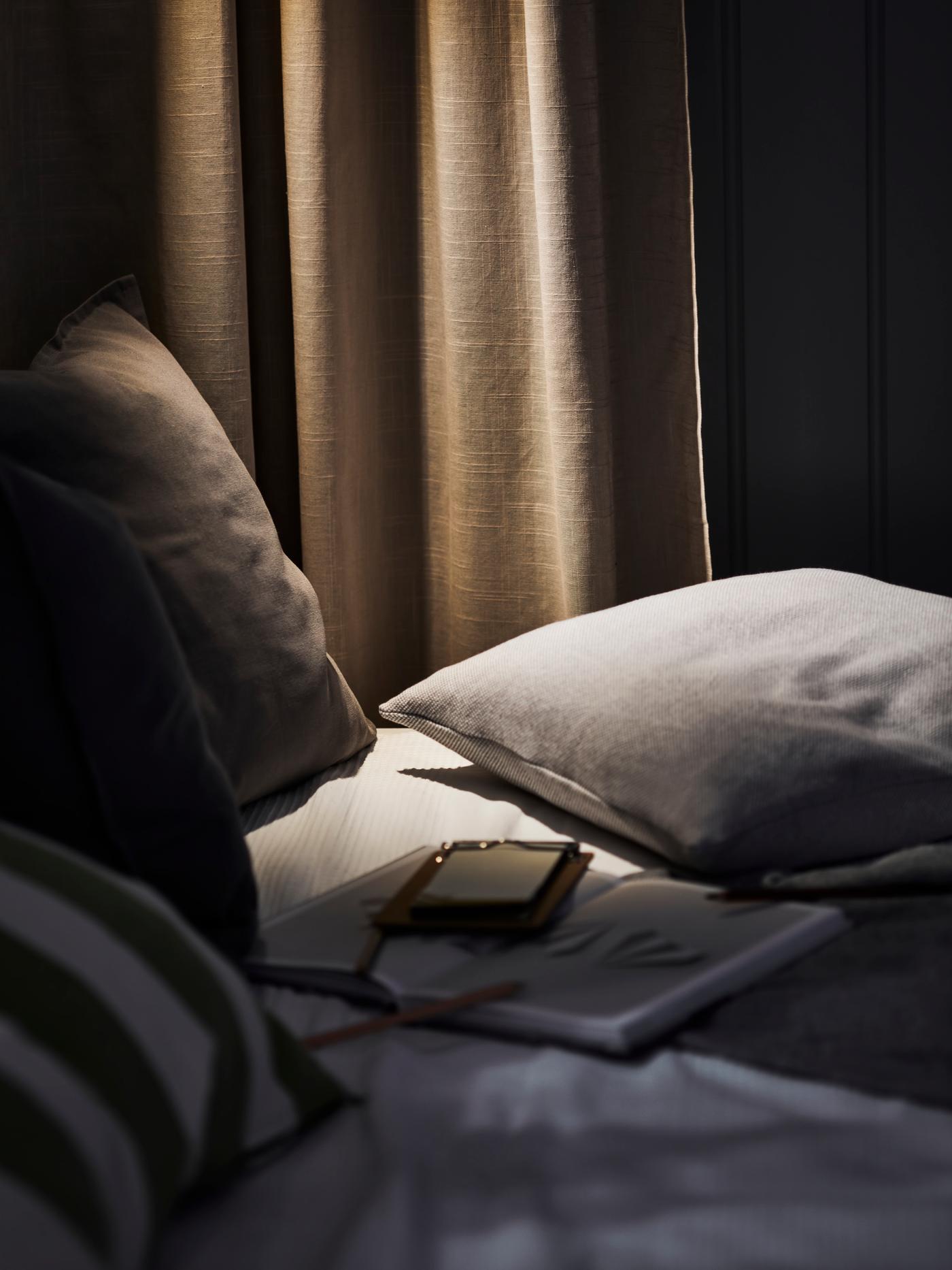 Cama donde hay un celular junto a cojines en una pieza oscura