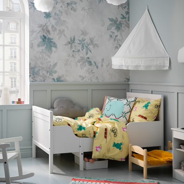 Cama para niños o infantil SUNDVIK blanca, con cubrecamas amarillo con dibujos en una pieza con muebles y adornos blancos.