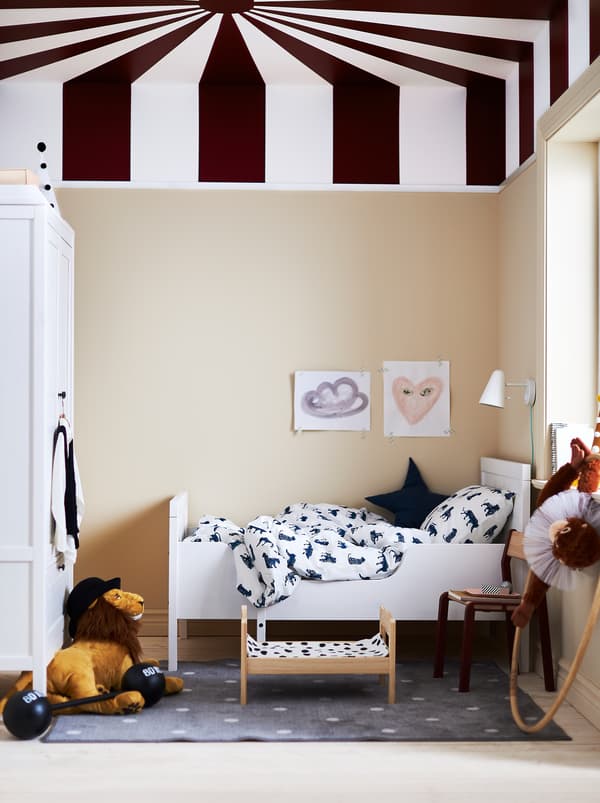 Cameretta con il soffitto dipinto a righe per ricordare il tendone di un circo, letto allungabile SUNDVIK bianco e biancheria da letto bianca e blu scuro.