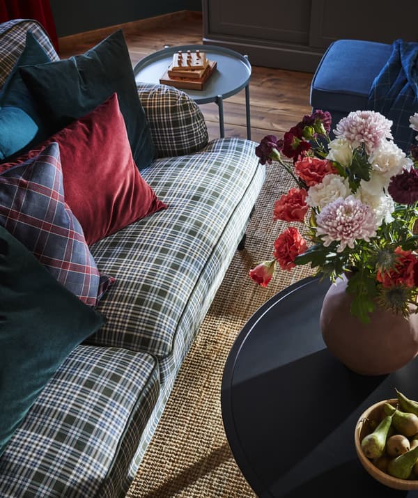 Canapé à motif tartan et coussins colorés, tables d’appoint et vase garni de fleurs, vus d’en haut.