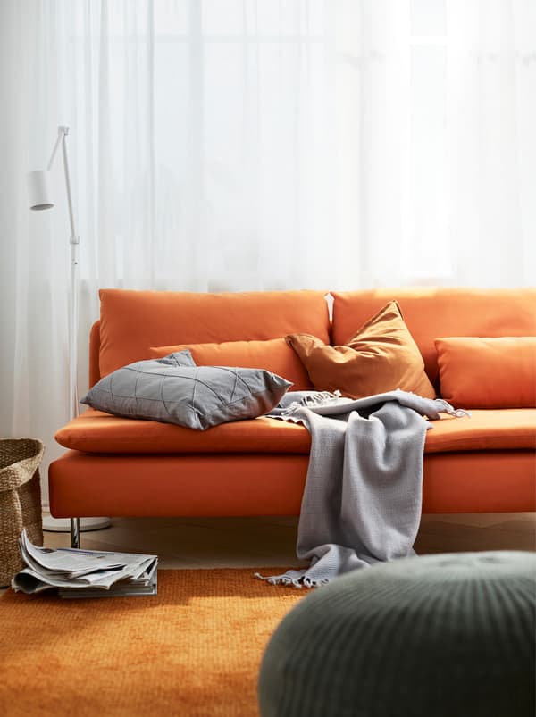 Canapé à trois places orange SÖDERHAMN avec coussins et jeté dans un salon avec un gros tapis orange.