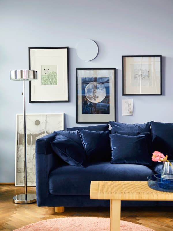 Canapé en velours bleu avec affiches tropicales sur le mur du fond. GIF montrant de nouveaux coussins dans des couleurs claires ajoutés à un canapé.