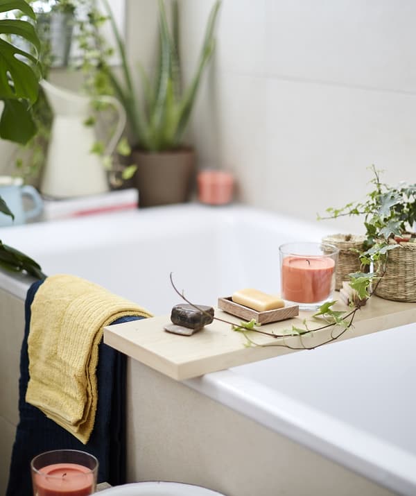 Candles, soap and plants on a wooden board laid across a bath.