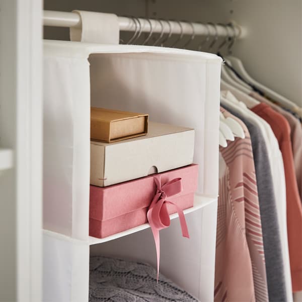 Cardboard boxes stacked inside a hanging organiser next to clothes on a rail.