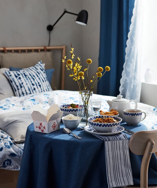 Cared-for dinner-for-one setting with oriental-style, multi-bowl meal on a small round table next to a bed.