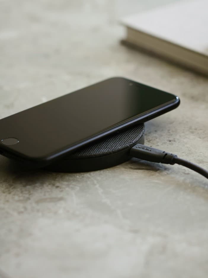 Černý smartphone položený na bezdrátové nabíječce IKEA LIVBOJ na stole.