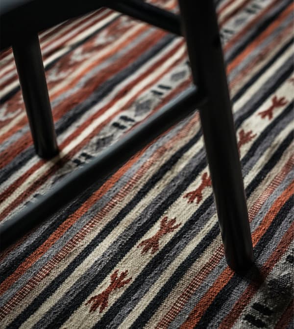 Chaise de salle à manger noire posée sur un tapis tissé à rayures.