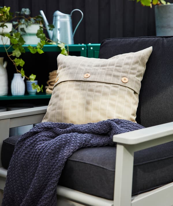 Chaise d’extérieur avec coussins bleu foncé, avec un coussin supplémentaire beige et une couverture bleu foncé.