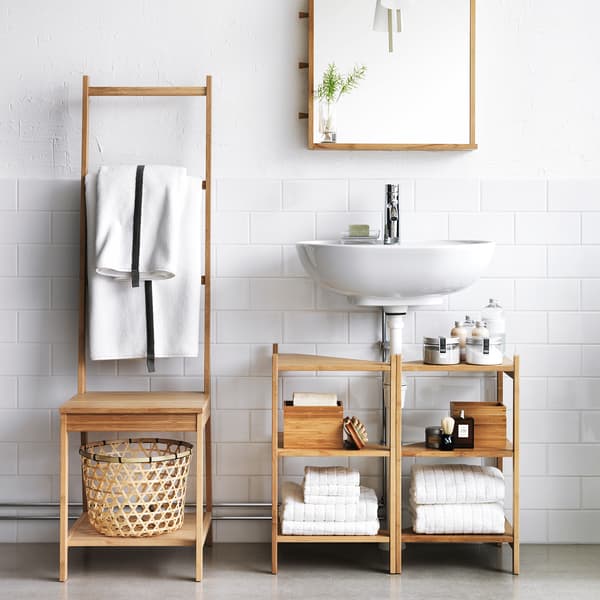 Chaise en bambou RÅGRUND avec porte-serviettes à côté de l’étagère d’évier en bambou RÅGRUND dans une salle de bain blanche.