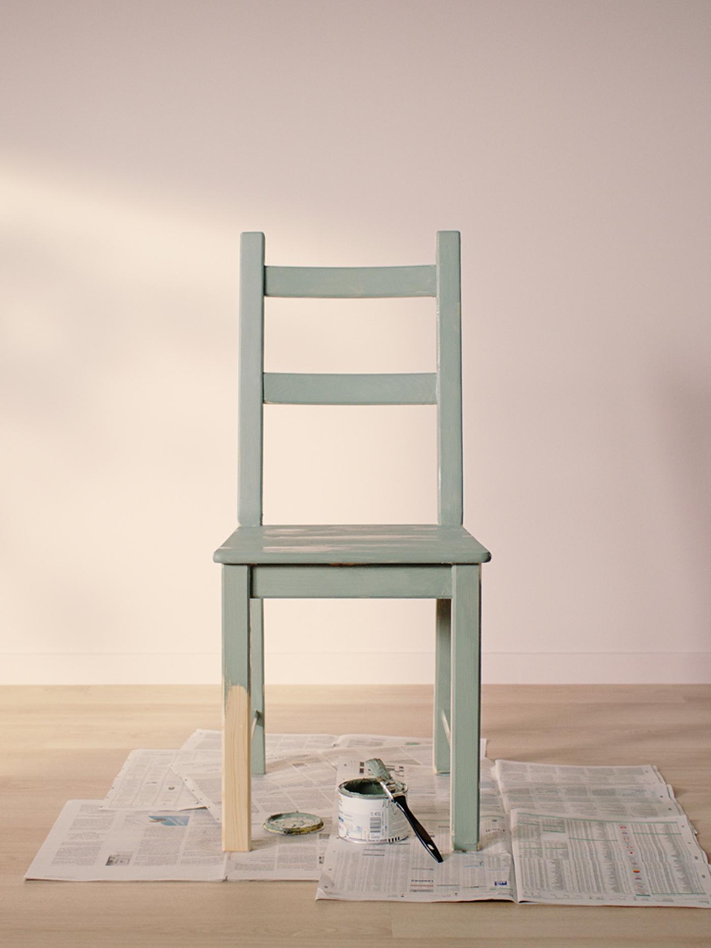 Chaise IVAR vert clair posée sur de vieux journaux dans une pièce vide au plancher clair et aux murs rose pâle.