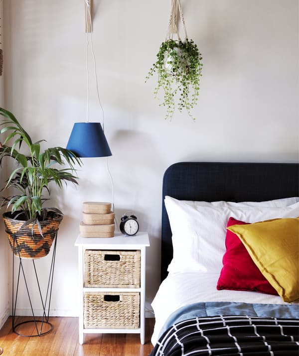 Chambre à coucher avec coussins colorés sur le lit, table d’appoint et plantes.