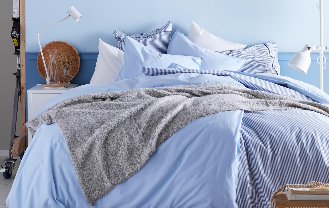 Chambre à coucher avec palette de couleurs en blanc et bleu, avec une profusion de couvertures et de coussins.