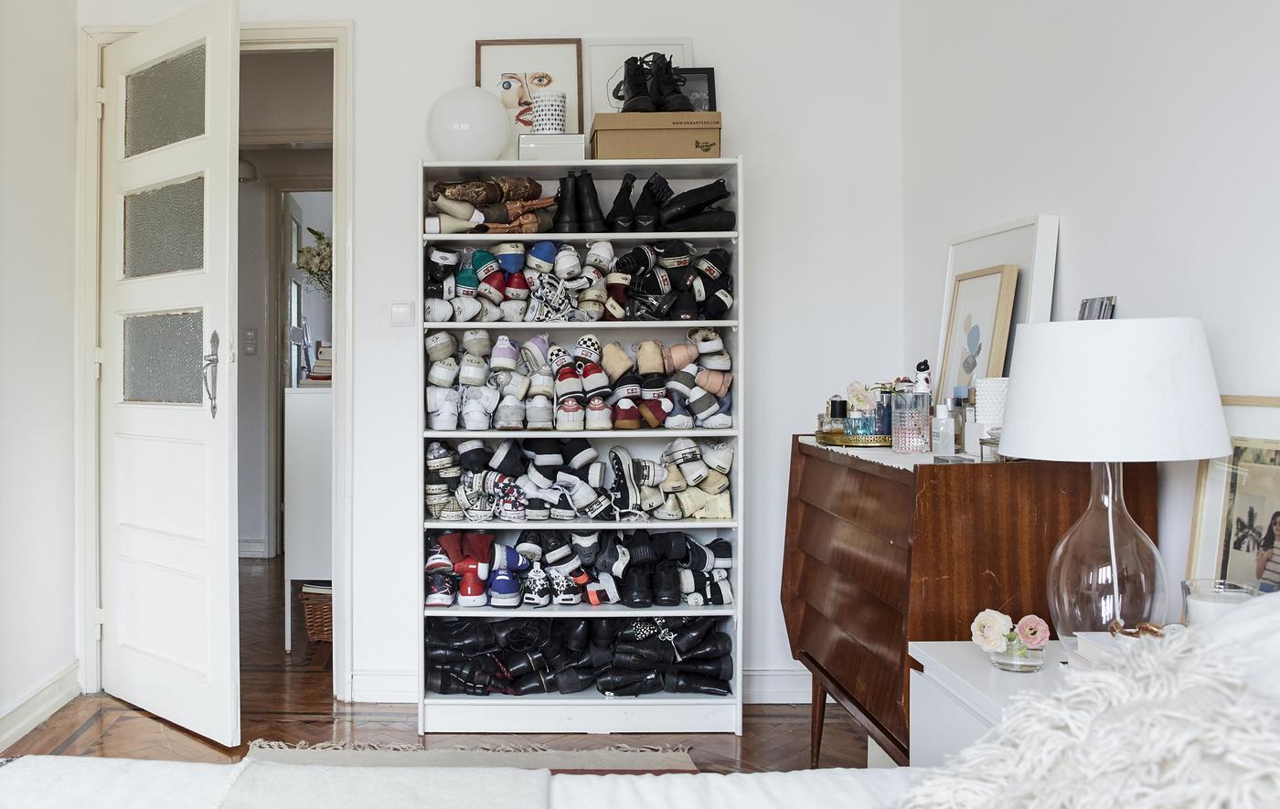 Chambre à coucher blanche avec parquet et chaussures empilées dans une bibliothèque.