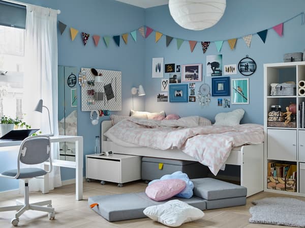Chambre à coucher d’ado avec murs bleus et lit SLÄKT blanc, avec rangements en dessous, à côté d’un bureau PÅHL et d’une chaise junior ÖRFJÄLL en blanc et gris.