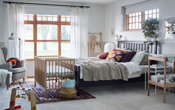 Chambre à coucher d’adulte en beige, brun, rouge et jaune avec petit lit et table à langer SNIGLAR en hêtre et blanc.