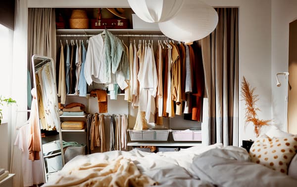 Chambre à coucher où des rideaux sont ouverts sur une large alcôve dans un mur, révélant une armoire-penderie bien remplie et misant sur des rangements BOAXEL.