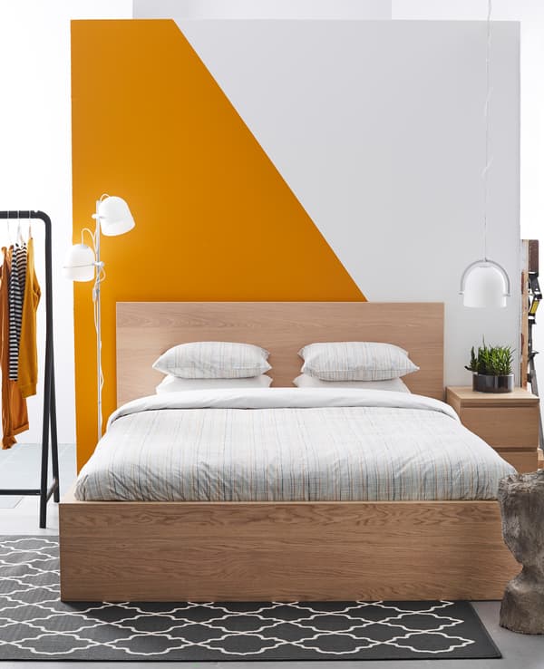 Chambre à coucher simple et sobre, avec motif graphique orange et blanc au mur.