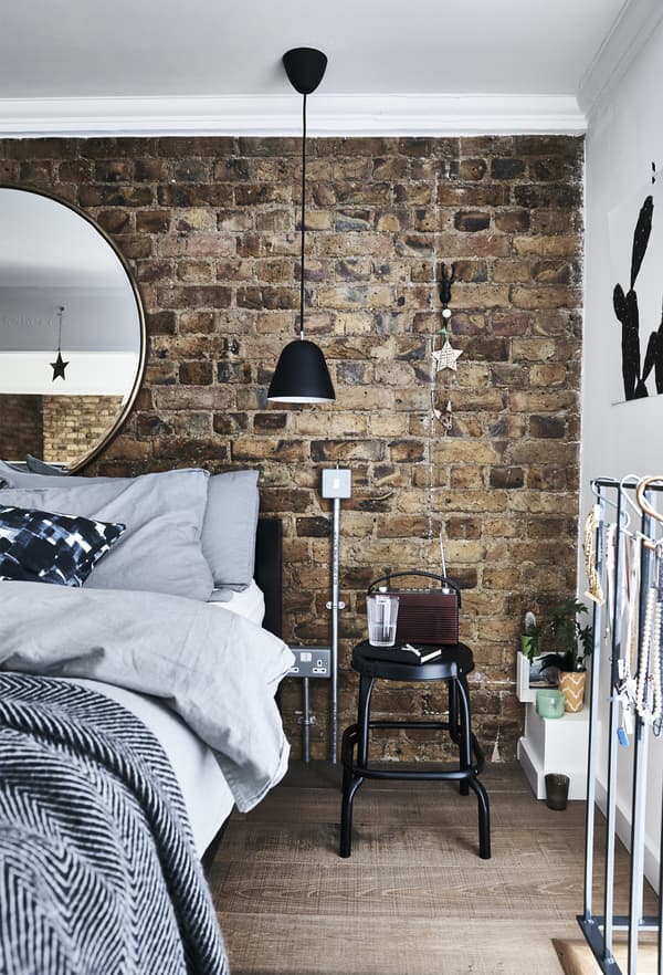Chambre avec mur en briques apparentes et linge de lit gris.