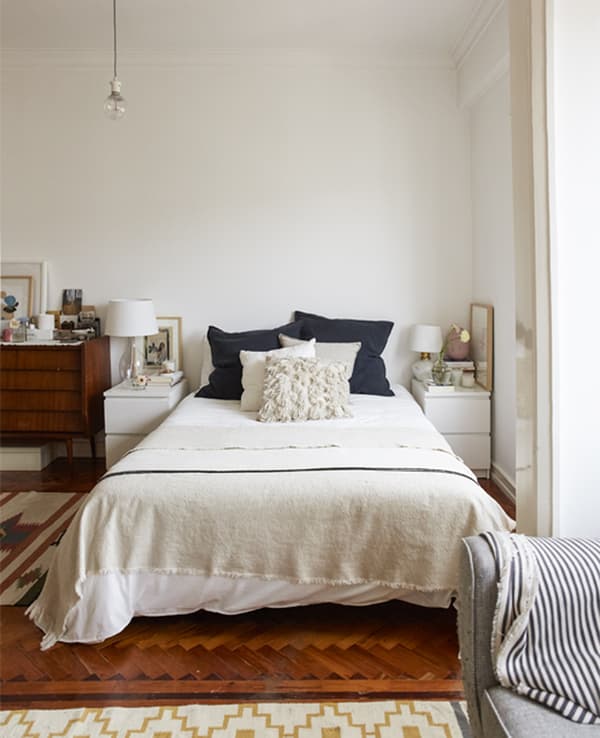 Chambre avec plancher en bois, murs blancs et plusieurs couches de textiles de lit.
