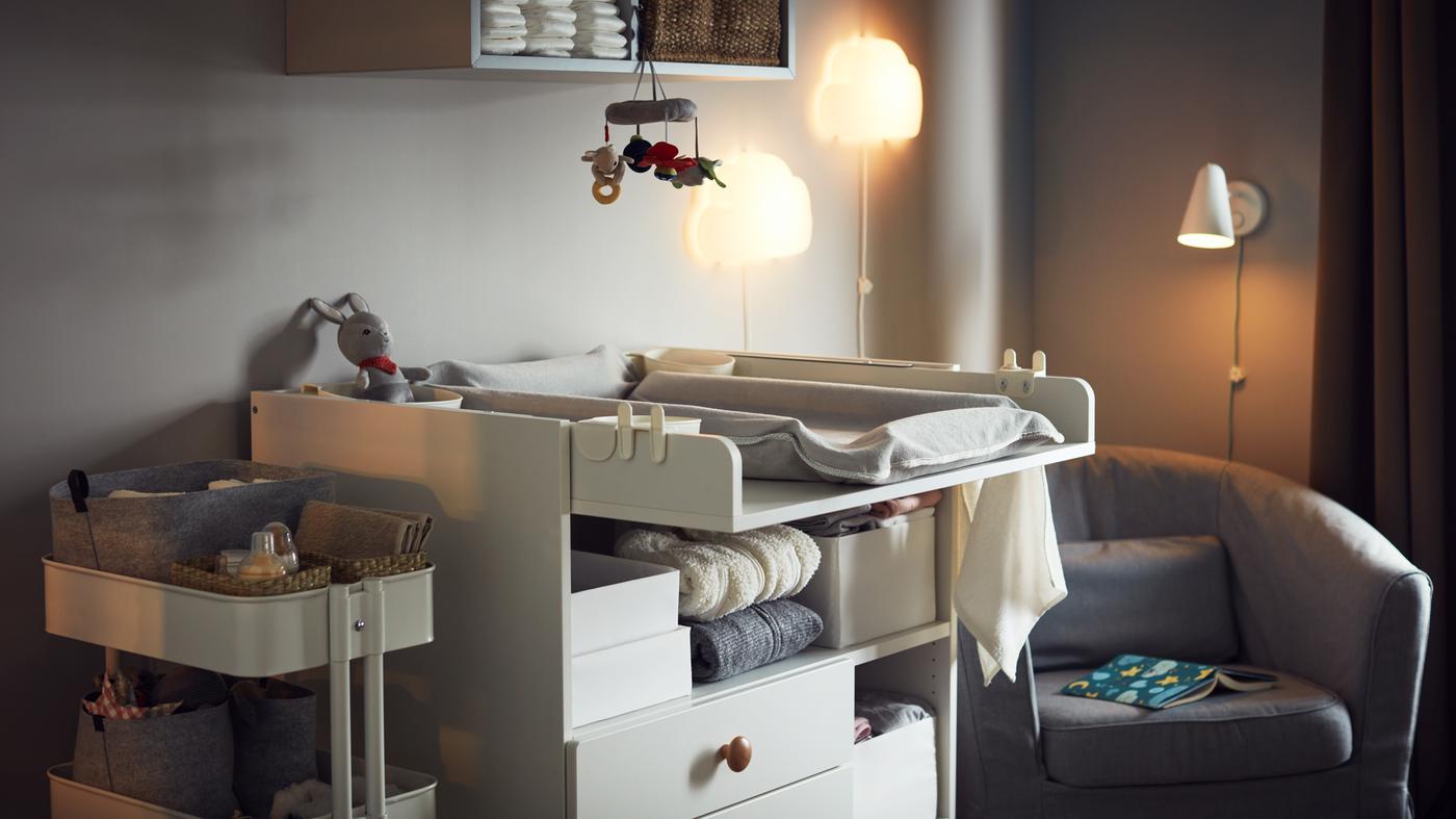 Chambre chaleureuse et douillette comportant une table à langer, une desserte avec accessoires pour bébé, un fauteuil confortable pour allaiter, des veilleuses murales et un rangement mural.